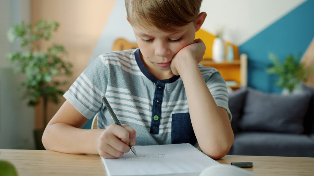 Young child writing in a notebook at a desk, representing creative writing prompts for kids