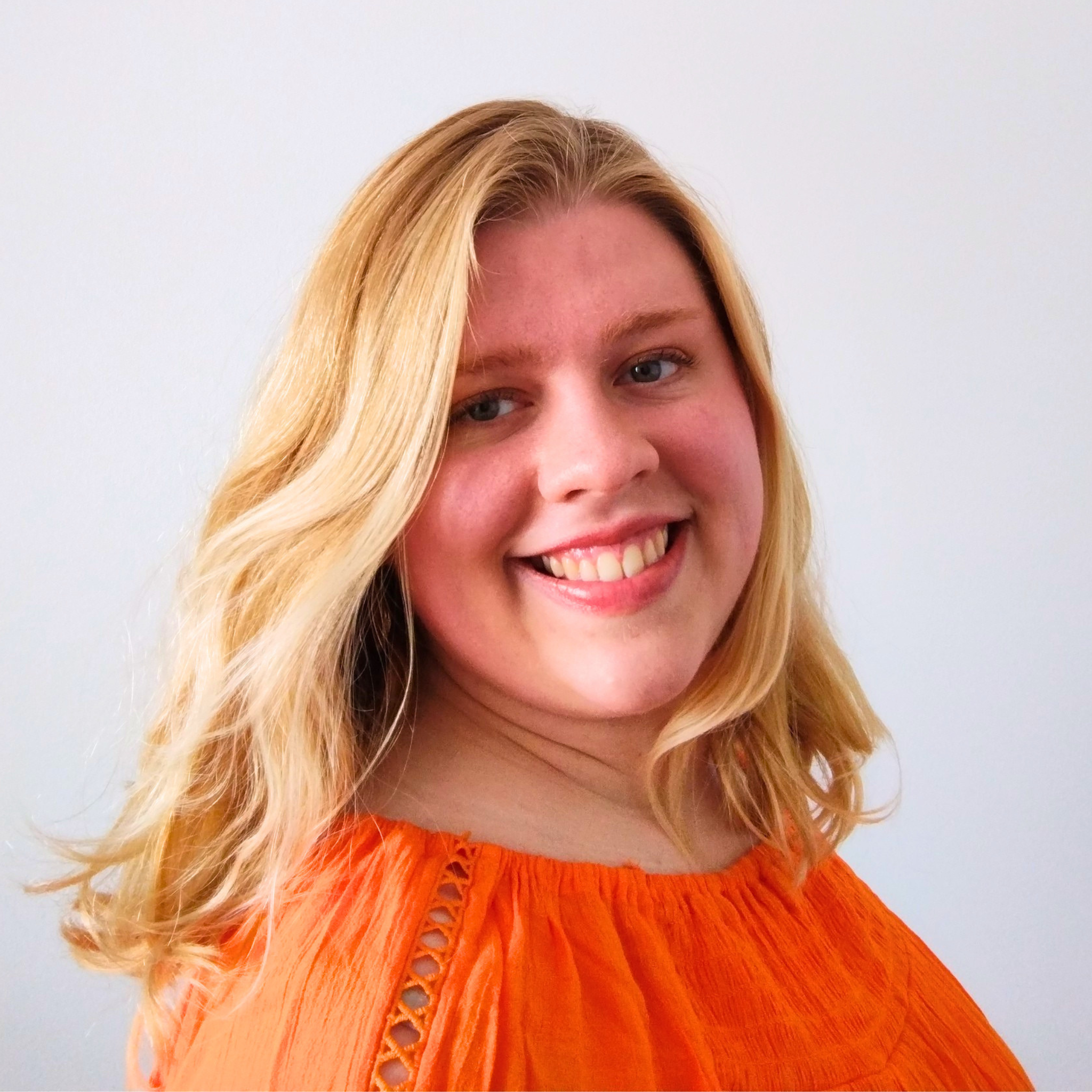 Author Grace Gidman smiling in a warm, natural headshot wearing an orange blouse against a soft neutral background